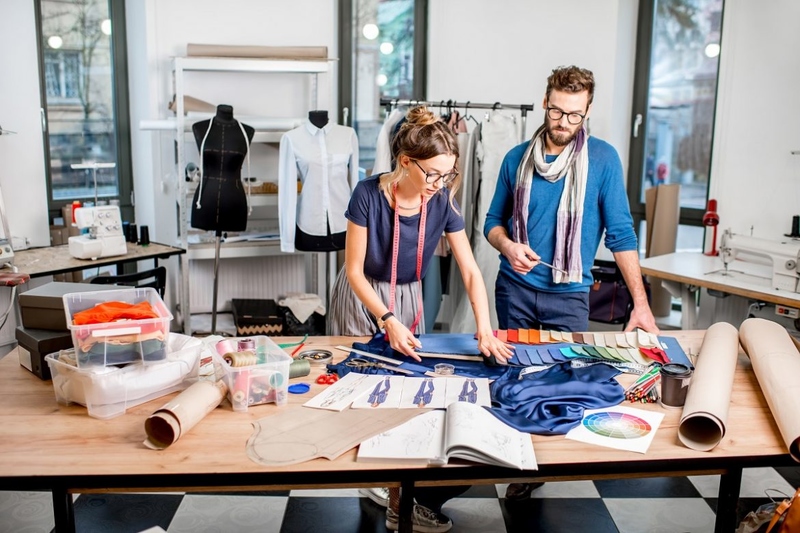 Imagem de dois estilistas. Eles estão desenhando roupas