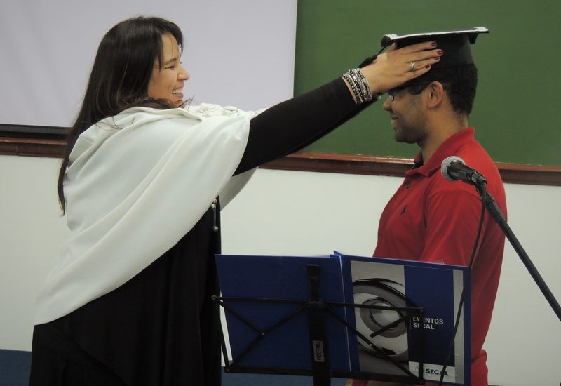 Na imagem se encontra a Pró-reitora da UniSecal colocando o capelo em um aluno da instituição.