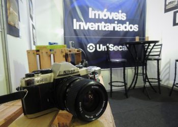 Imagem de uma câmera e ao fundo um banner do 'Imóveis Inventariados' da UniSecal.