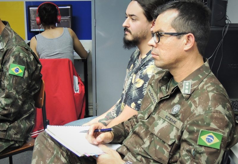 Imagem de um militar e de um aluno da UniSecal. Eles estão no laboratório de Jornalismo