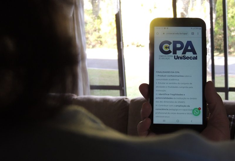 #PraCegoVer: Foto de uma mulher utilizando um celular e acessando o site da CPA UniSecal